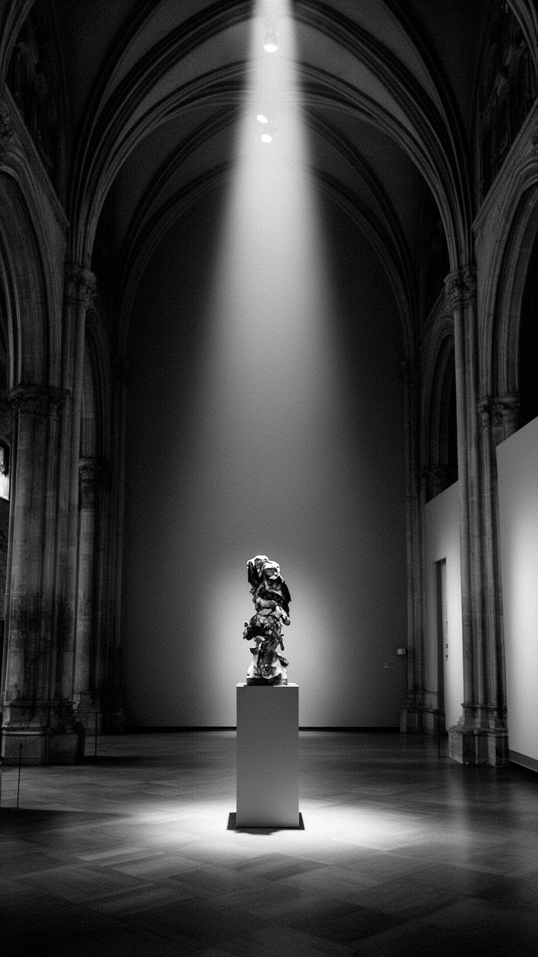 Cathedral-like gallery interior with a singular sculpture lit by a shaft of light